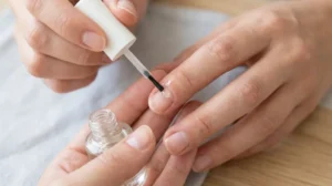 Woman applying cuticle oil to dry, damaged nails after gel polish removal.