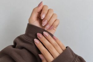 Dusty rose almond nails with soft white marble accents, paired with chocolate-brown sweatshirt sleeves.