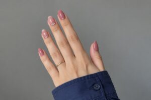 Dusty rose almond nails with tiny crystal accents, paired with a navy blue shirt cuff.