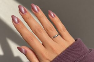 Dusty rose almond nails with a silvery cat eye shimmer in sunlight, paired with a muted plum sleeve.