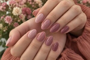Glossy almond nails in coordinated blush, dusty rose and mauve shades against a soft floral background.