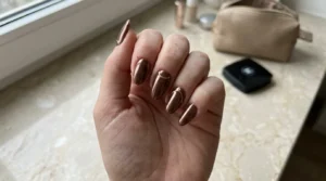 Close-up of brown chrome nails with delicate gold details