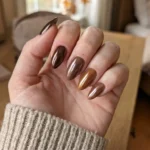 Close-up of glossy brown chrome nails in a cozy fall beauty aesthetic