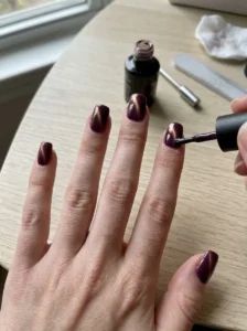 Woman applying an even layer of deep plum magnetic cat-eye polish to her nails