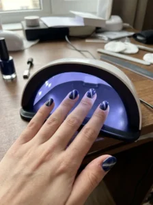 Woman curing navy blue cat-eye nails under a small UV LED nail lamp