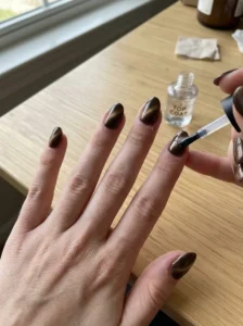 Woman applying a clear top coat over glossy brown cat-eye nails