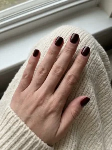 Short glossy black cherry nails on a natural-looking hand