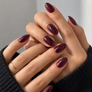 Deep plum jelly nails on overlapping hands with a thin gold ring.