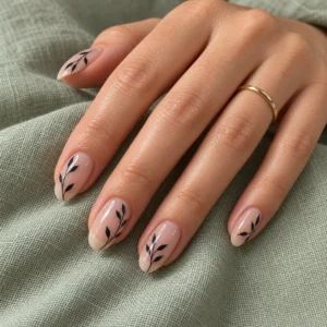 Delicate black leaf designs over sheer nude-pink nails on sage green linen.