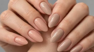 Peach beige and warm nude nail polish on fair-skinned hands resting on pale stone.