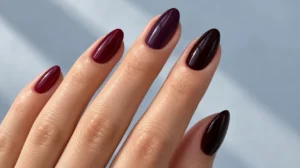 Glossy burgundy, plum, and black cherry almond nails on a fair-skinned hand.