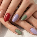 Fair-skinned hands with rosy nude, peach, red, lilac, and sage green nails.