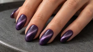 Violet almond nails with lavender cat eye shimmer resting on a charcoal surface