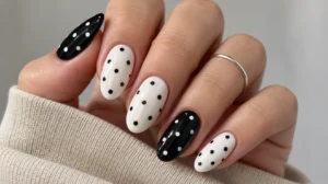 Black-and-white almond nails with contrasting polka dots beside a beige sleeve.