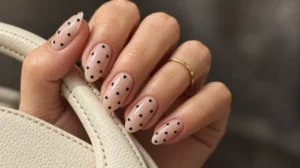 Nude almond nails with black polka dots on a hand holding an ivory handbag strap.