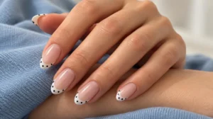 Nude-pink almond nails with tiny black polka dots on white French tips.