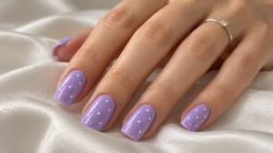 Glossy lilac nails with tiny white polka dots resting on ivory satin.
