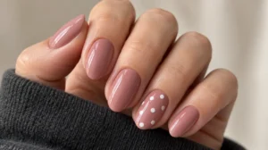 Dusty rose nails with white polka dots on a single ring-finger accent nail.