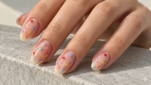 Clear glossy oval nails decorated with small multicolored polka dots.