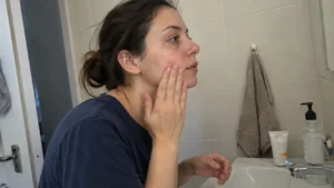 Woman gently applying moisturizer beside her bathroom sink.