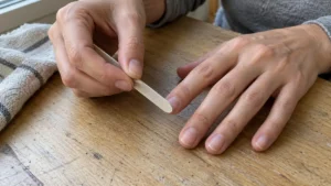 Woman filing her short natural nails with an emery board at a wooden table.
