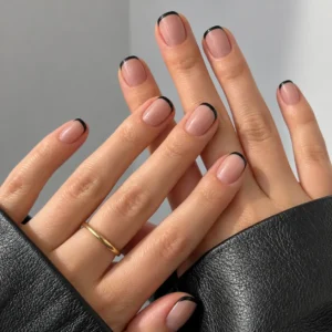 Close-up of overlapping hands with short nude-pink nails and thin black French tips