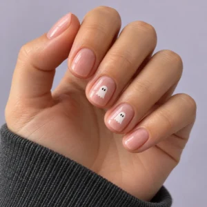 Close-up of short blush-pink nails with tiny white ghosts on two accent nails against a pale lavender background.
