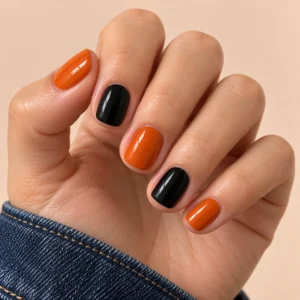 Close-up of short squoval nails painted alternating glossy black and pumpkin orange against a pale peach background.