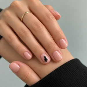 Close-up of short nude-pink nails with a small black cat silhouette on the ring fingernail.
