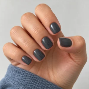 Close-up of short squoval nails with smoky charcoal-gray polish against a clean ivory background.