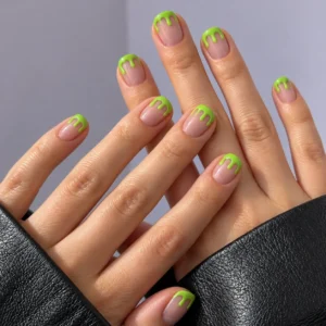 Close-up of short nude-pink nails with bright green dripping slime tips against a lavender-gray background.
