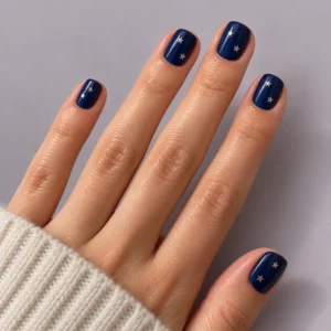 Close-up of short midnight-blue nails with tiny silver stars against a pale mauve background.