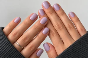 Close-up of overlapping hands with glossy milky lavender nails against a clean ivory background.
