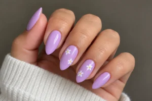 Close-up of lavender almond nails with tiny white daisies and yellow centers on two accent nails.