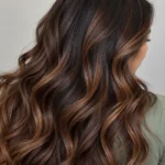 Close-up of dark honey brown hair with subtle warm highlights and large flowing waves, viewed from behind.
