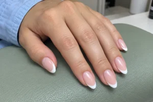Close-up of almond-shaped French nails with pink bases and white tips resting on a sage manicure cushion.
