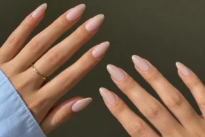 Close-up of two hands with pink-to-nude ombré almond nails and fine champagne shimmer at the tips.