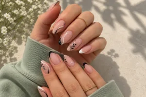 Nude pink almond nails with delicate black and white curves, leafy accents, tiny dots, and a white outline heart.