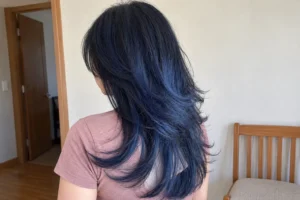 Rear three-quarter view of layered blue-black hair with feathered ends and a navy sheen, worn with a dusty-rose top.