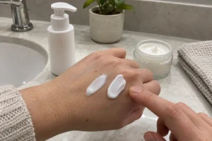 Lightweight lotion and thick cream swatches on the back of a hand beside moisturizer containers.