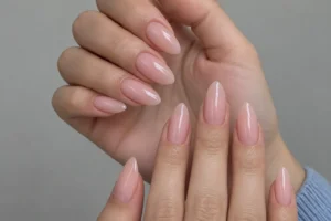 Close-up of two hands with glossy sheer blush pink almond nails against a pale gray background.