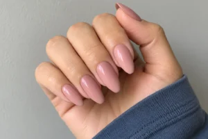 Close-up of glossy dusty rose almond nails with a slate blue sleeve against a light gray background.