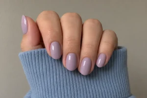 Close-up of glossy creamy lavender oval nails resting over a soft blue ribbed sleeve.