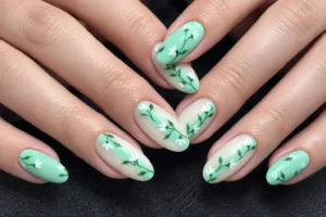 Close-up of mint green and milky ivory almond nails with delicate white flowers and green leafy stems.