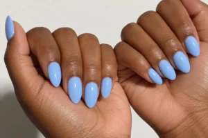 Close-up of two curled hands with glossy powder blue almond nails against an off-white background.