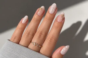 Close-up of pearl white almond nails with shell-like shimmer, blush accents, and delicate gold leaf details.