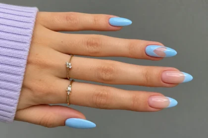 Spring manicure with pastel blue almond nails, blue French tips, nude accents, and delicate gold rings.