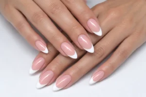 Two overlapping hands with glossy baby pink almond nails and white French tips on a white surface.