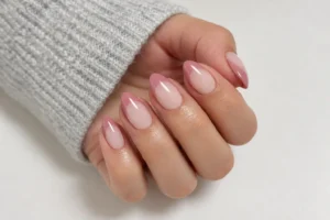 Close-up of almond nails with sheer pink bases and dusty rose French tips beside a light gray knitted sleeve.