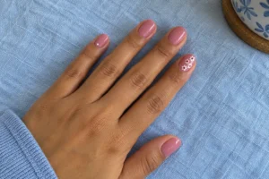 Glossy cool pink oval nails with small white flower accents resting on light blue fabric.